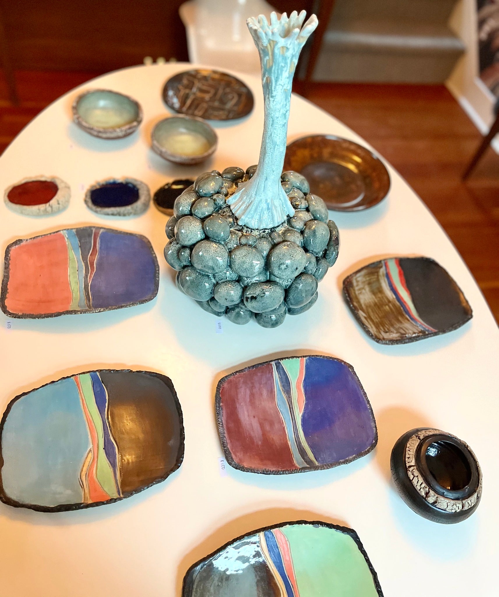 Collection of so-q ceramic plates and a central vase on a white table.