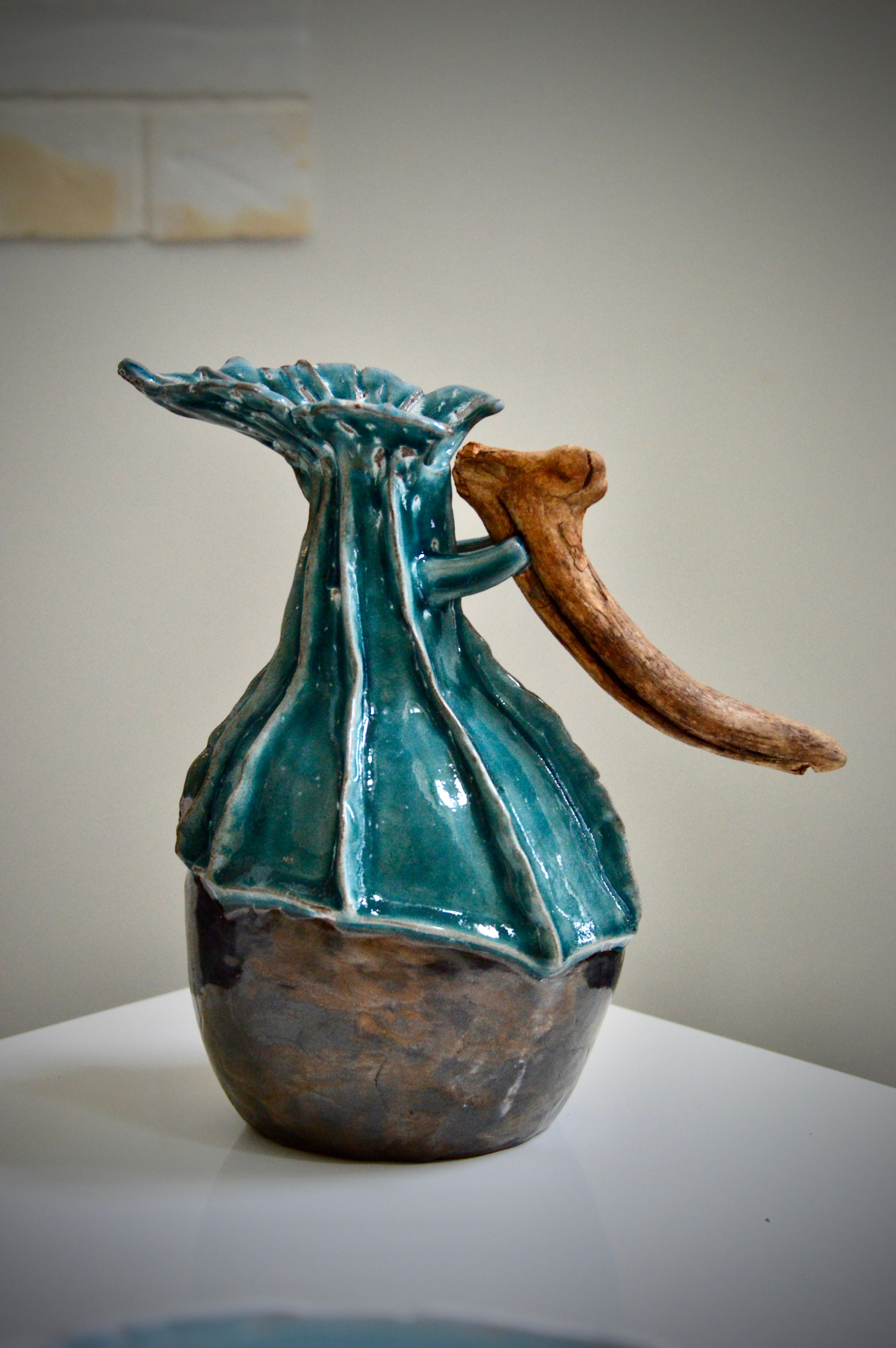 Ceramic pitcher with a natural branch handle on a plain surface