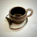 Ceramic bronzed cup with handle and saucer on a white surface