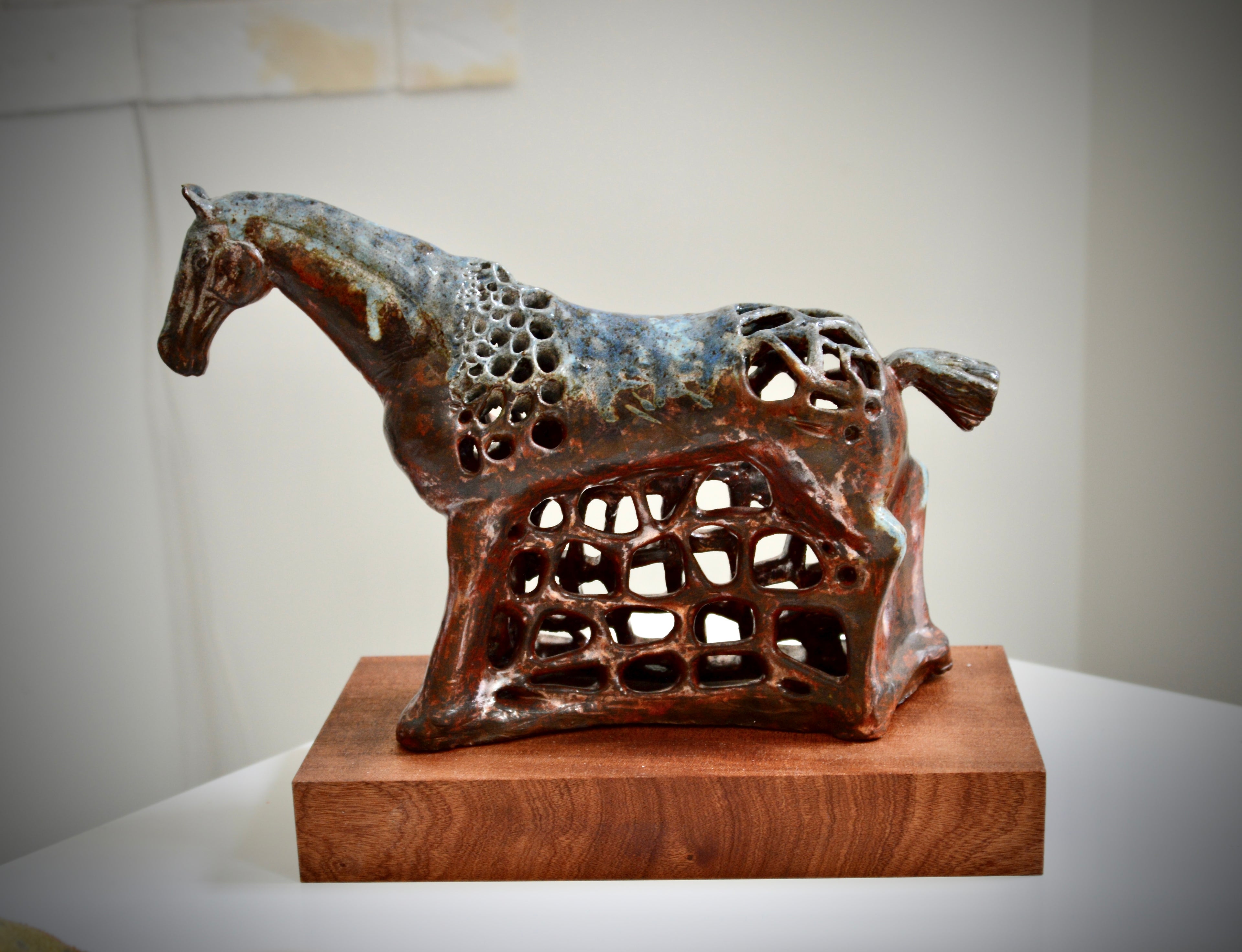 Ceramic horse sculpture on a wooden base against a plain background