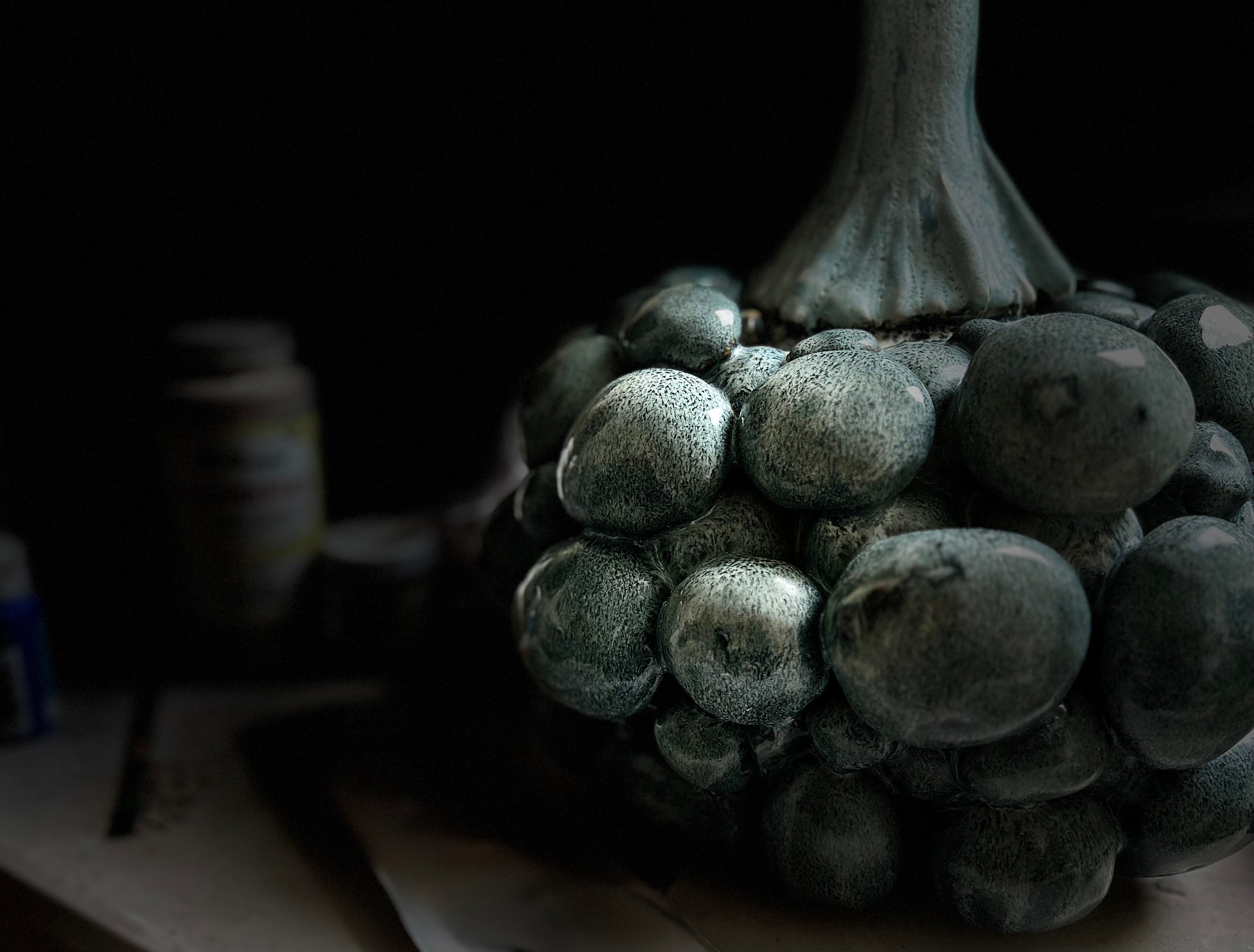Dark, textured ceramic object resembling a cluster of fruits or vegetables on a dark background