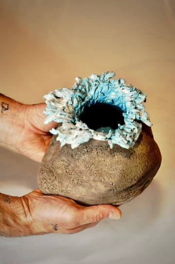 Hand holding a stone vase with turquoise coral-like top against a plain background