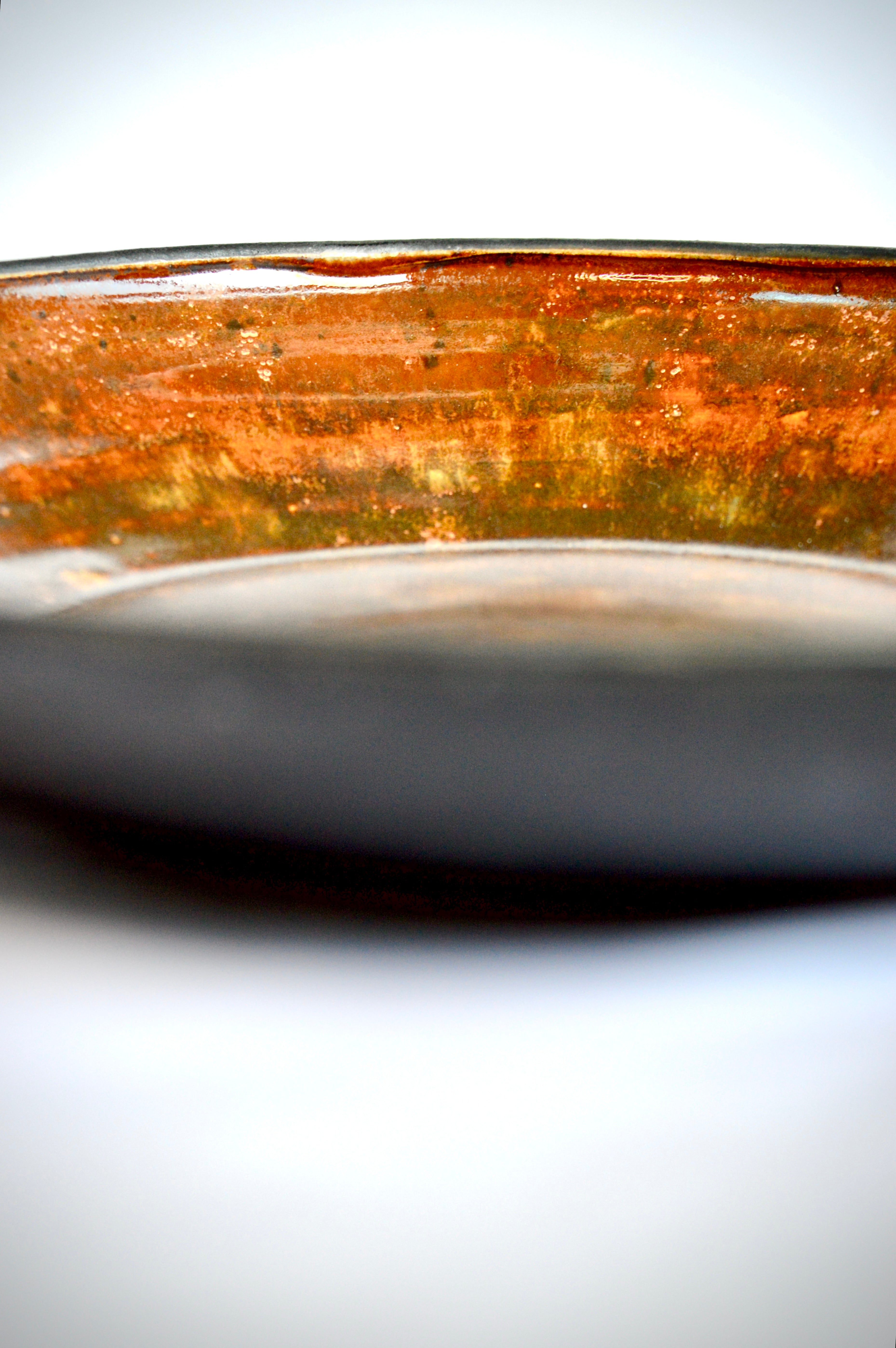 Close-up of an orange coloured ceramic bowl with a metallic rim on a white background