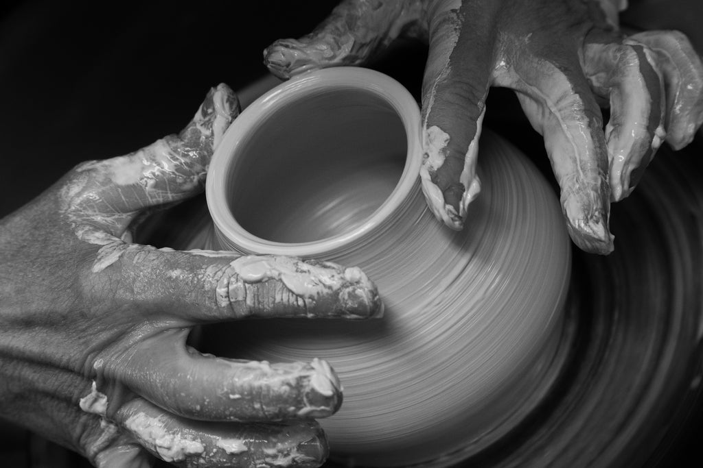 Black and white image of hands working with clay on a potter's wheel