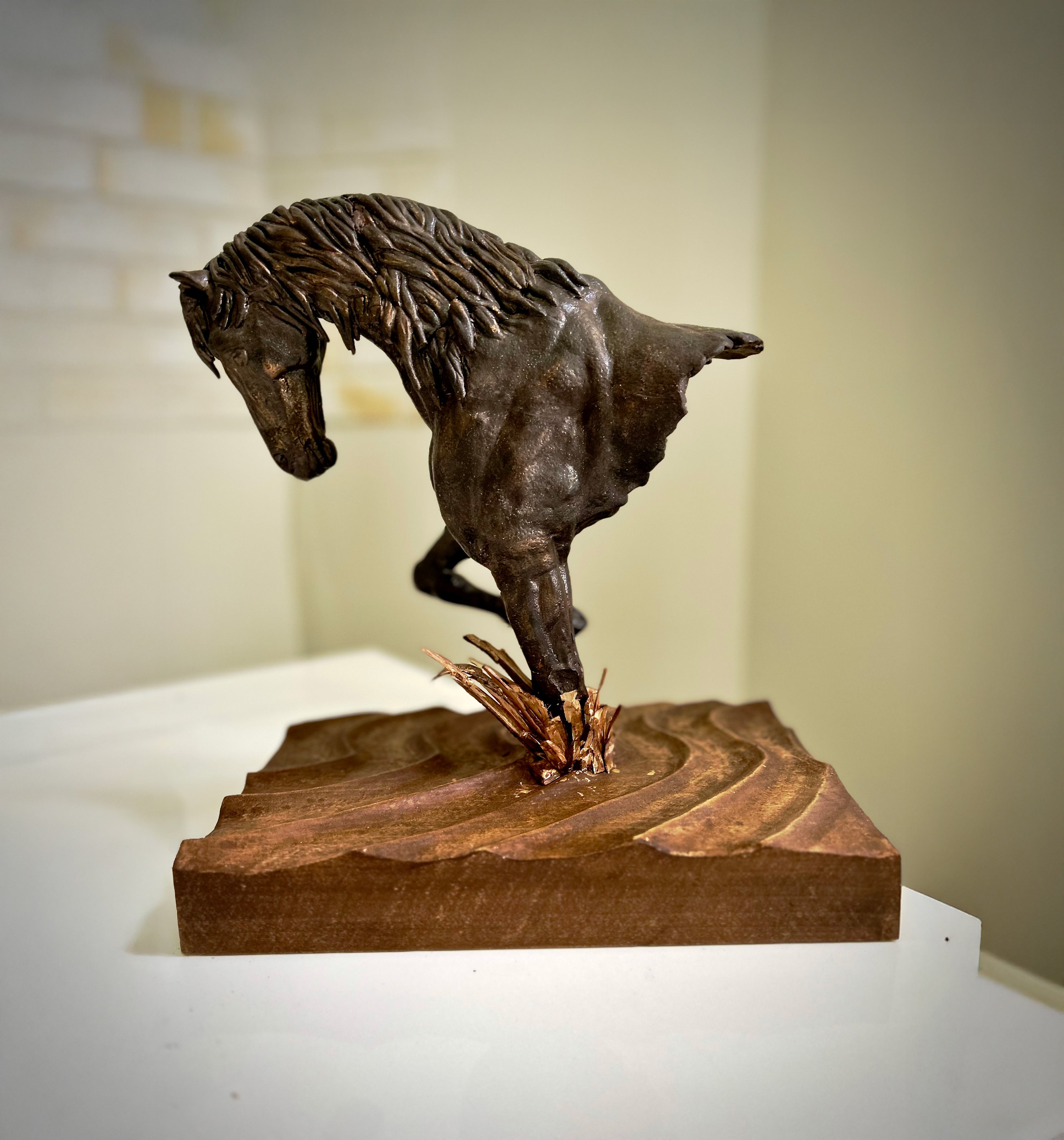 Bronze sculpture of a horse on a wooden base against a neutral background