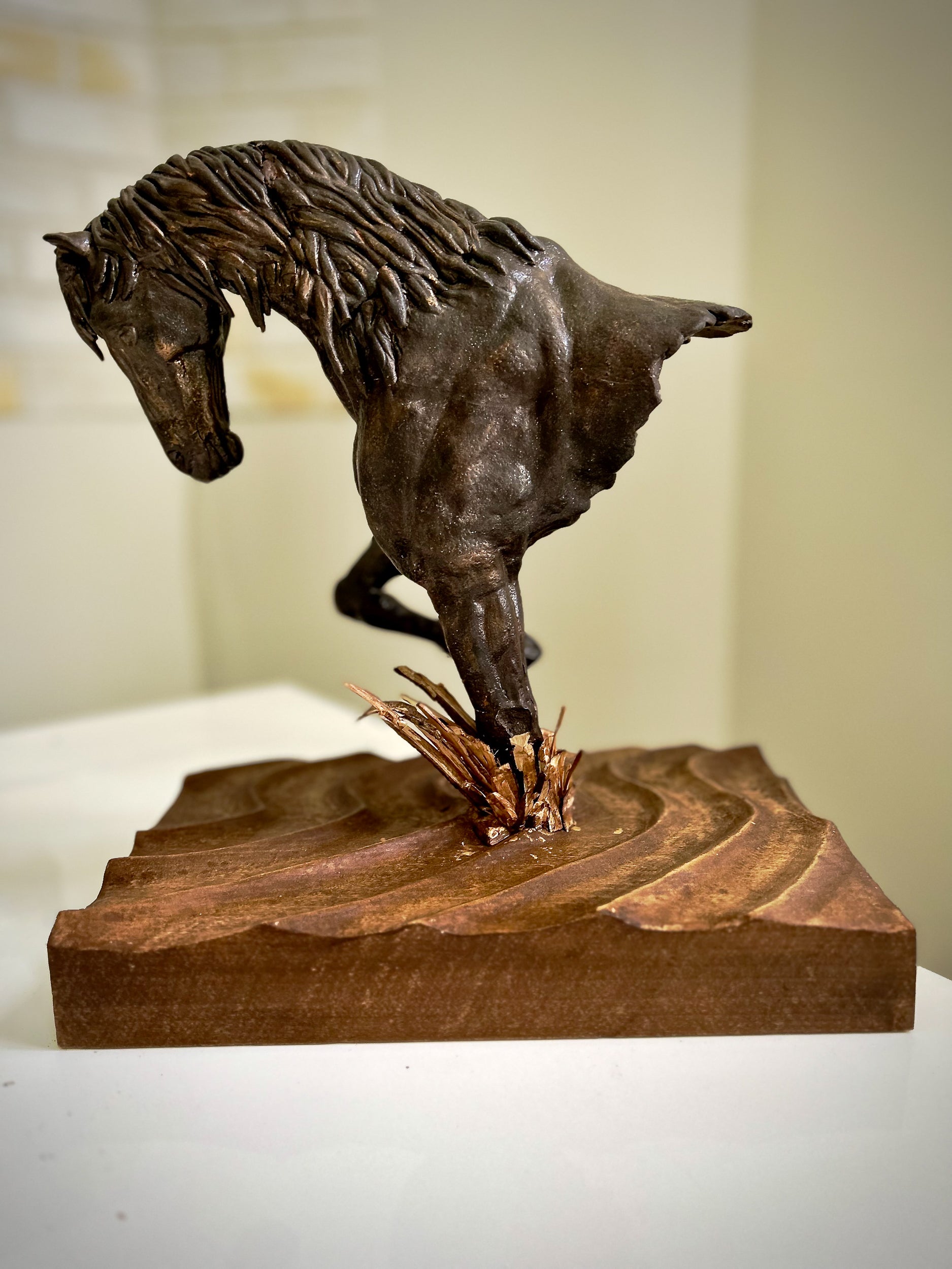 Bronze sculpture of a horse rearing on a wooden base against a neutral background